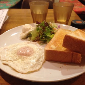 Café da manhã ocidentalizado - café com leite, pão, ovo, salada e um copo d'água.